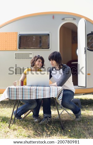 Young couple with laptop in front of camping trailer