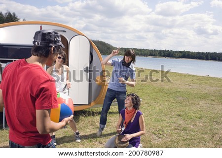 Young people relaxing by lake in front of camping trailer