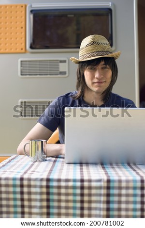 Young man with laptop in front of camping trailer