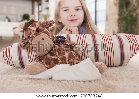 Girl with a stuffed toy smiling lying on carpet
