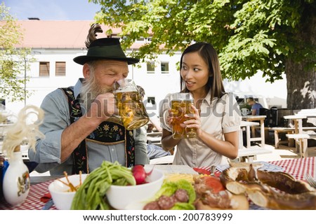 Germany Bavaria Upper Bavaria Bavarian man and Asian woman drinking beer in beer garden