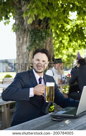 Germany, Bavaria, Upper Bavaria businessman in beer garden holding beer mug smiling