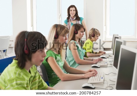 In computing class teacher standing students using computer wearing headphones