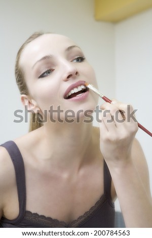 Young woman applying lipstick, portrait, close-up