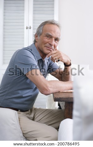 Senior man sitting at table hand on chin looking at camera