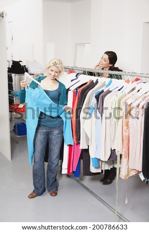 Two women in fashion shop woman showing friend trousers