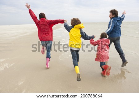 Germany, St. Peter-Ording, North Sea family holding hands and running on beach rear view