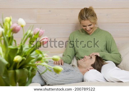 Couple relaxing on sofa man lying in woman's lap woman stroking his head smiling