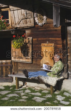 Austria, Karwendel, senior man sitting in front of log cabin reading a book