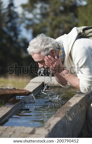Mature man washing face from water well