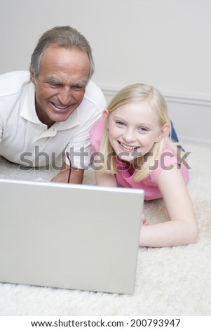 Grandfather and granddaughter lying on floor using laptop smiling