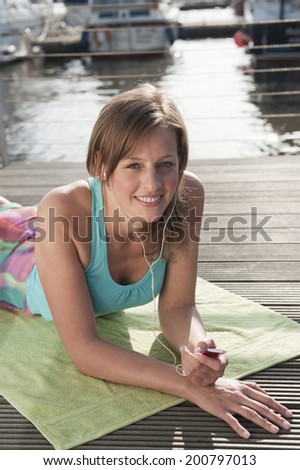 Germany, Hamburg, Woman lying on sun deck listening to music