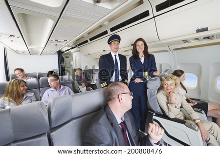 Flight captain and stewardess standing in between passengers of business class airplane cabin