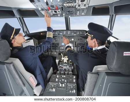 Pilot pushing button in airplane cockpit with co-pilot
