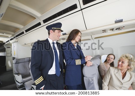 Flight captain and air hostess talking with passengers on airplane