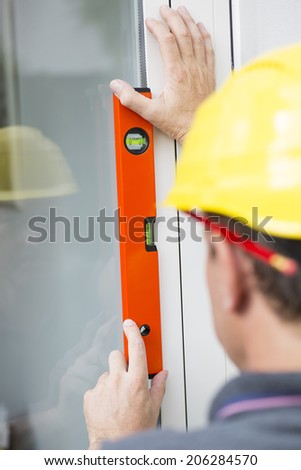 Construction worker measuring window\'s straightness with spirit level