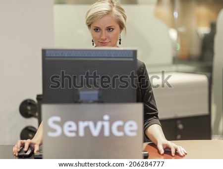 Blond woman working at help desk looking at the screen Freiburg Germany