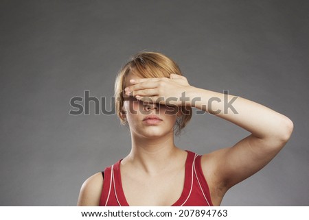 Teenage girl in red tank top covering eyes against gray background