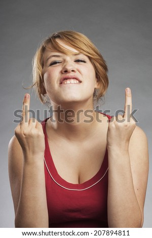 Teenage girl in red tank top showing obscene gesture against gray background