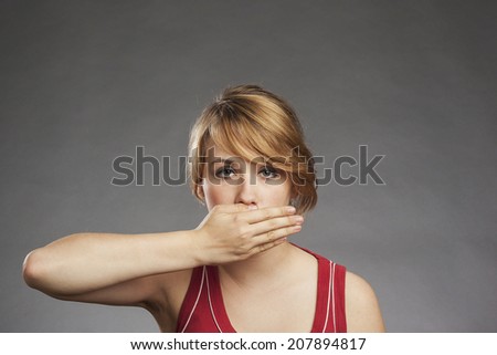 Teenage girl in red tank top covering eyes against gray background