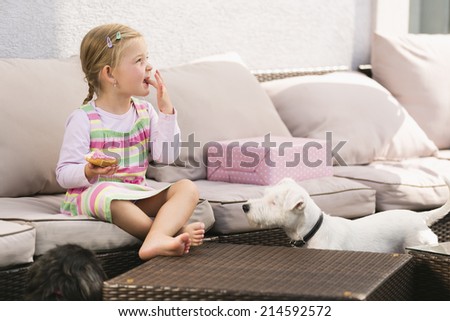 Young girl eating doughnut dog waiting next to her