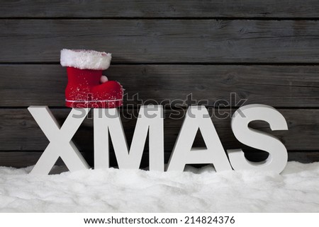 Capital letters forming the word xmas on top santa\'s boot on pile of snow against wooden wall