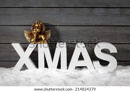 Capital letters forming the word xmas and golden putto figurine on pile of snow against wooden wall