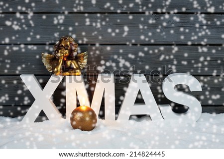 Capital letters forming the word xmas golden putto figurine and candle on pile of snow against wooden wall snow is falling