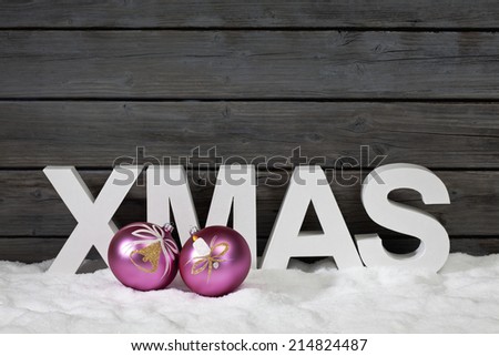 Capital letters forming the word xmas and christmas bulbs on pile of snow against wooden wall