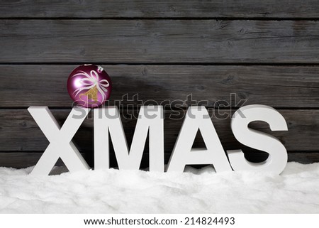 Capital letters forming the word xmas on top christmas bulb on pile of snow against wooden wall