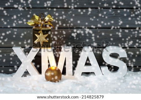 Capital letters forming the word xmas with star shaped decoration above on pile of snow against wooden wall snow is falling