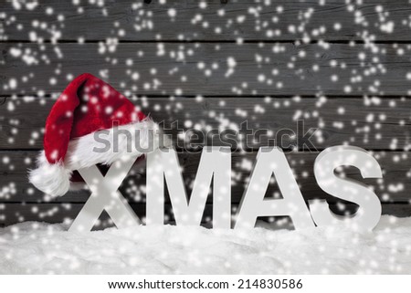 Capital letters forming the word xmas and christmas hat on pile of snow against wooden wall
