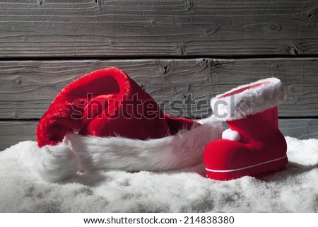 Christmas hat and boot on heap of snow against wooden background