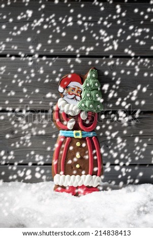Snowfall with gingerbread santa claus on heap of snow against wooden background