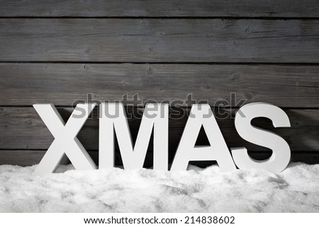 Capital letters forming the word xmas on pile of snow against wooden wal
