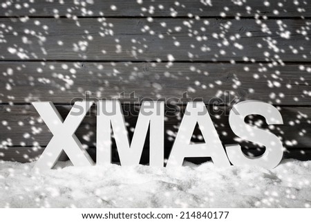 Capital letters forming the word xmas on pile of snow against wooden wall snow is falling