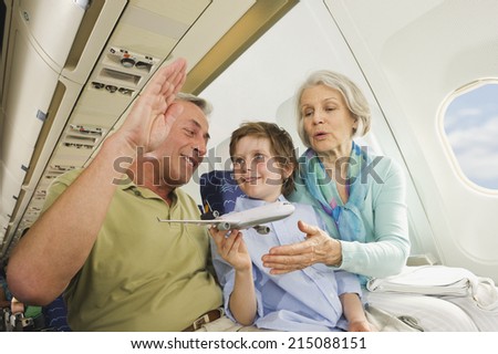 Boy holding model airplane besides senior man and woman on airplane