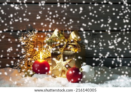 Golden christmas present, christmas ball, candle on pile of snow against wooden wall