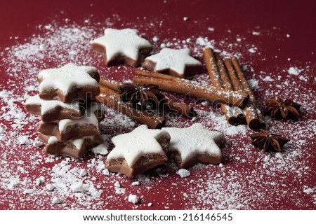 Cinnamon stars and spices sprinkled with powder sugar on red background