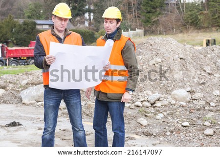 Project manager and architect standing in construction site looking at blueprint