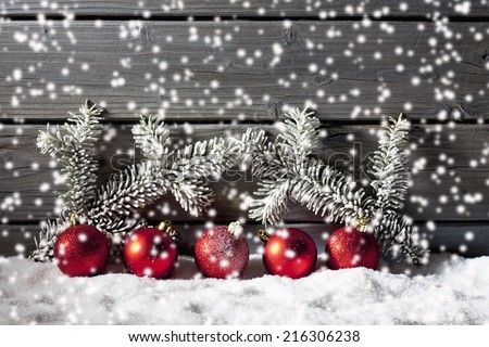 Red christmas ornaments on pile of snow against wooden wall
