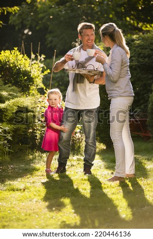 Family in garden, fahter and mother drinking coffee daughter embracing father's leg