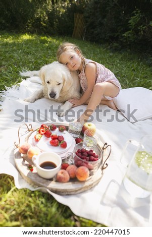 Girl sitting with golden retriever on blanket in garden having picnic