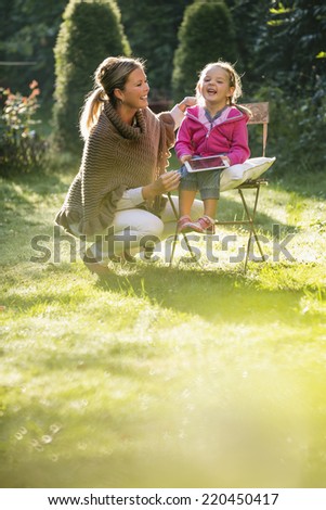 Young girl sitting on chair in garden mother crouching next to her