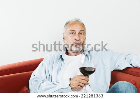 Senior man sitting on couch holding wine glass with red wine in hand