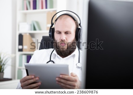 Doctor reading on digital tablet, weraing headphones