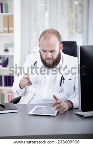 Doctor using digital tablet, drinking coffee