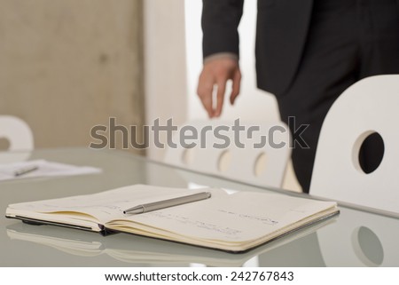 Notebook and pen on a desk, man in the background