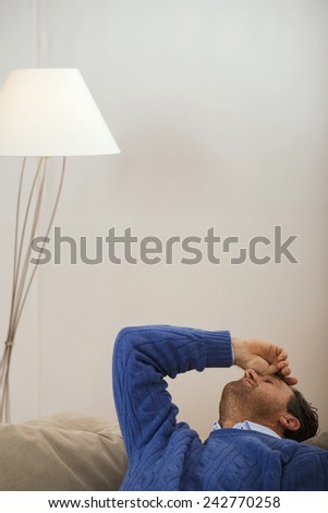 Man sitting on sofa, hand on head