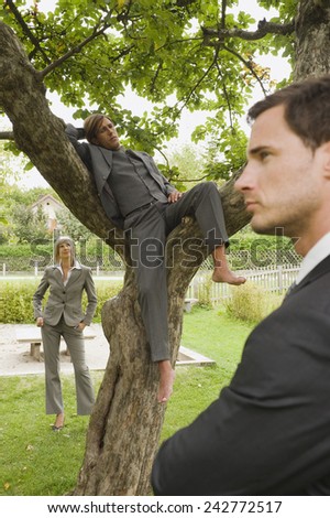 Germany, business people standing under tree, man sitting on branches